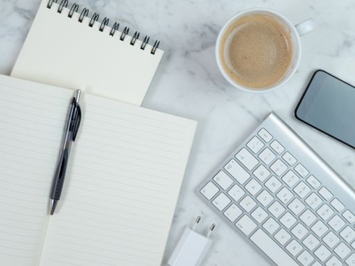 A top view closeup of the notebook, coffee, smartphone, and keyboard on the table