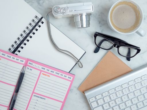 A top view closeup of the notebook, planner, eyeglasses, keyboard,coffee, and camera on the bed- concept planning a travel