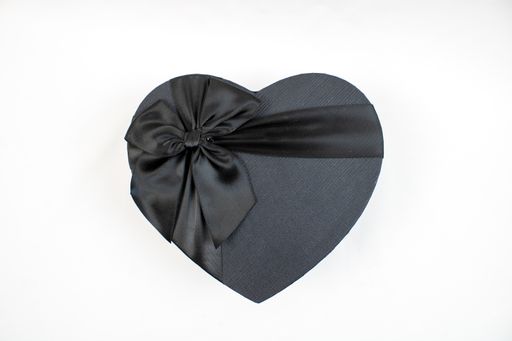 A top view shot of a black heart shaped gift box on a bright surface