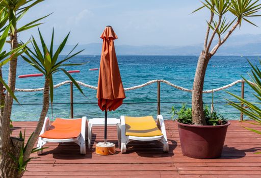 An orange beach umbrella and lounge chairs in a relaxing environment by the sea