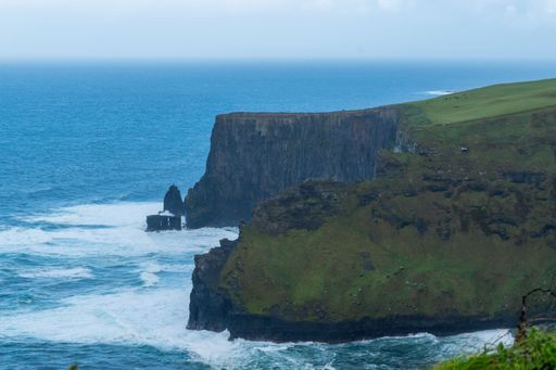 A lush, green grassy field with gentle waves lapping against the cliffs on a cloudy day