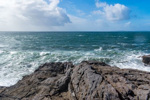 A lush, green grassy field with gentle waves lapping against the cliffs on a cloudy day