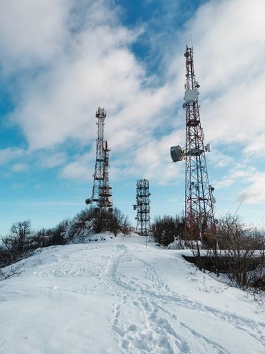 A snowy way taking to mobile towers on background of the cloudy blue sky