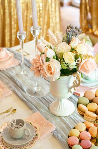 A vertical top view of a dessert table with beautiful tea time utensils and colorful macarons