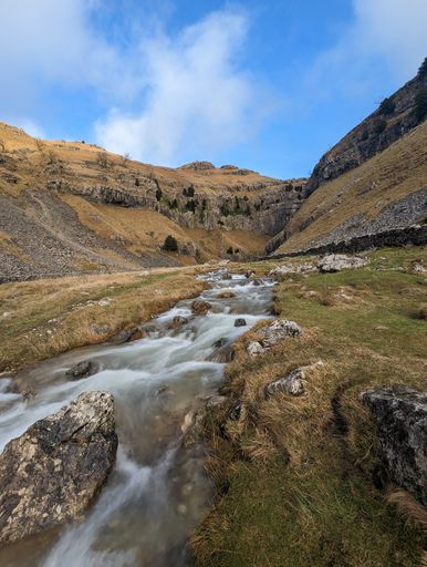 A majestic stream cascading down a lush valley surrounded by verdant, rolling hills