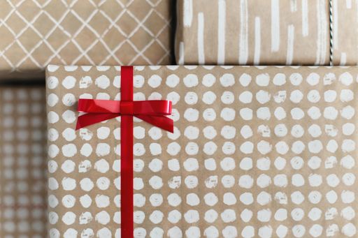 A closeup of a brown gift box with white round particles and a red ribbon on it