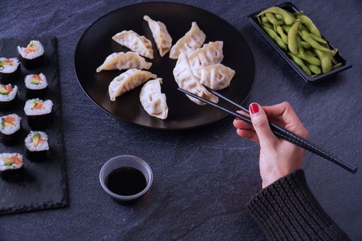 A high angle shot of a female hand about to take chicken gyozas, the salmon and avocado makis, endamame beans, and soy sauce served on the table