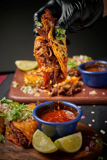 A vertical closeup of a hand dipping freshly made tacos in hot sauce