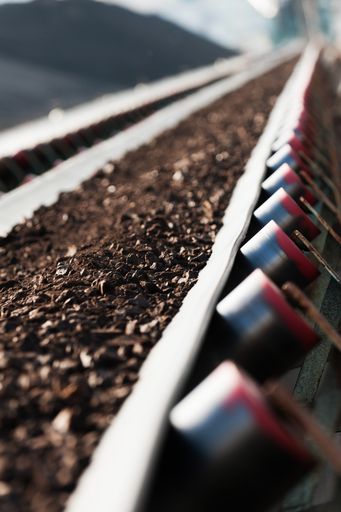 A vertical shot of coal being transported by a rubber conveyor belt with a blurry background