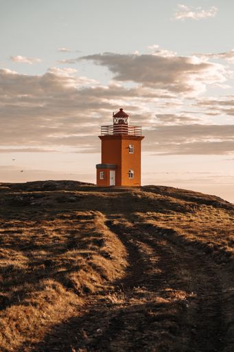 A vertical shot of a lighthouse under the cloudy beautiful sky on the rock in Iceland
