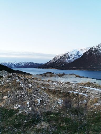 A scenic view of a fjord lake in Ersfjordbotn, Norway with a snowy mountain background