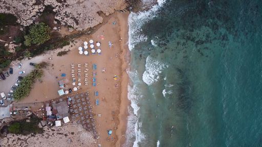 An aerial top-view shot of a clear seascape and a beach full of umbrellas