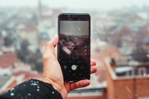 A closeup of a man hand taking a picture in the snow with his phone