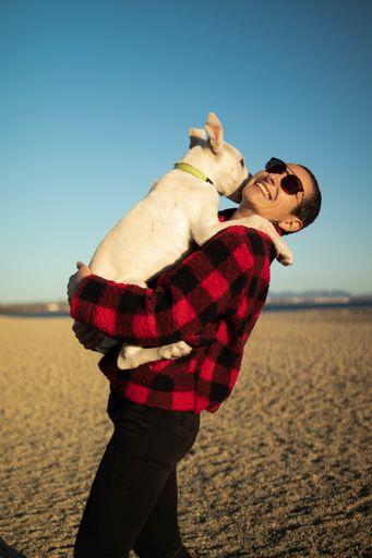 A shallow focus shot of a female with sunglasses playing with her white dog on the beach