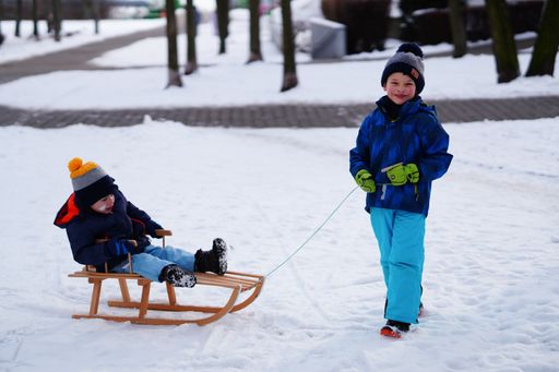 Boy pulling small child sitting on a wooden sled on snow on a cold winter day.