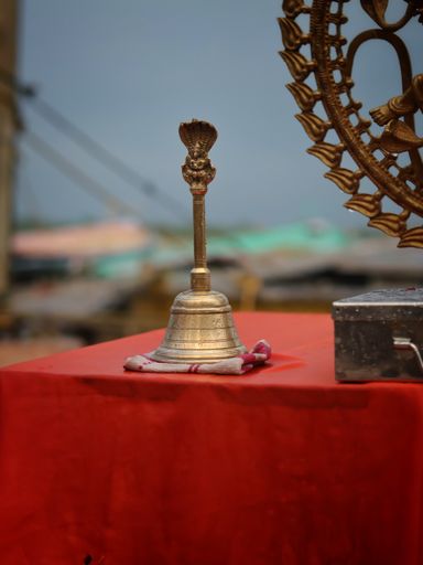 Closeup of a bell on a table wrap  with red cloth and Brass made statue of Lord Natraj with water droplets near Ganges river in Varanasi, India