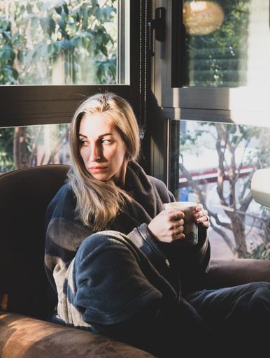 A young blonde female sitting in armchair and drinking coffee in the sunlight