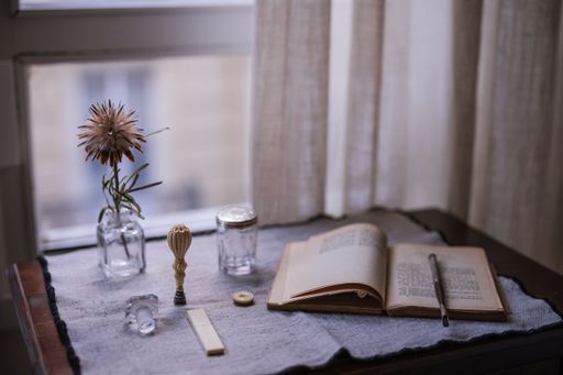 A closeup shot of an opened book near a flower in a vase near the window
