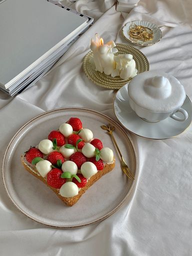 A vertical shot of strawberries, mozzarella cheese and basil on a toast near a cup of coffee