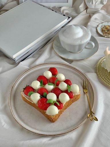 A vertical shot of strawberries, mozzarella cheese and basil on a toast near a cup of coffee