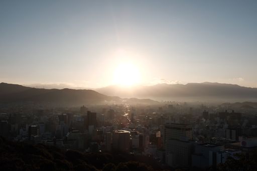 A city surrounded by hills covered in greenery under a blue sky during the sunset