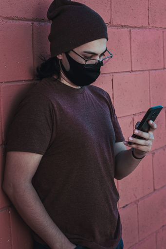 A vertical shot of a handsome caucasian male in glasses and facial mask looking at his phone - new normal concept