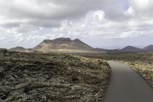 A curvy road surrounded by hills under a cloudy sky in Timanfaya National Park in Spain