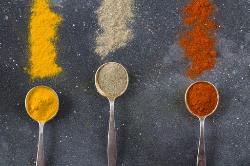 A top view closeup of the variety of spices on the vintage silver spoons on a blue background