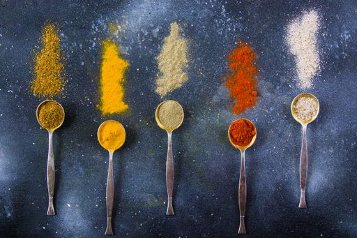 A top view closeup of the variety of spices on the vintage silver spoons on a blue background
