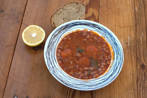 A high angle shot of a bowl of delicious bean soup with a slice of bread and half a lemon