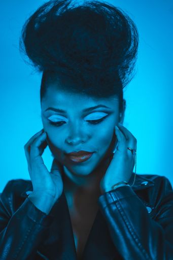 A closeup of a cool fashion hipster girl in a black leather jacket posing at the camera in blue lights