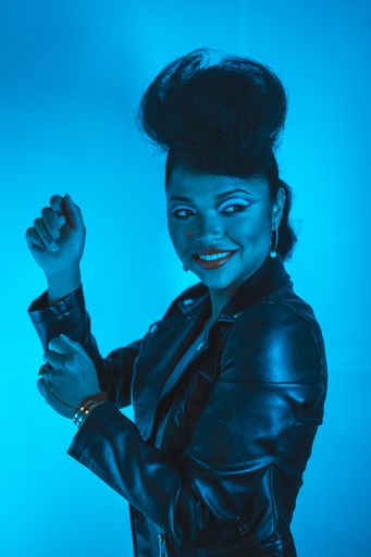 A vertical shot of a young pretty hipster female in a black leather jacket posing at the camera in blue lights