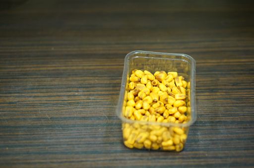A high angle closeup shot of salted corn in a plastic bowl on a wooden surface