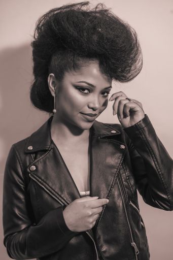 A vertical grayscale of a cool fashion hipster girl wearing a leather jacket posing at the camera