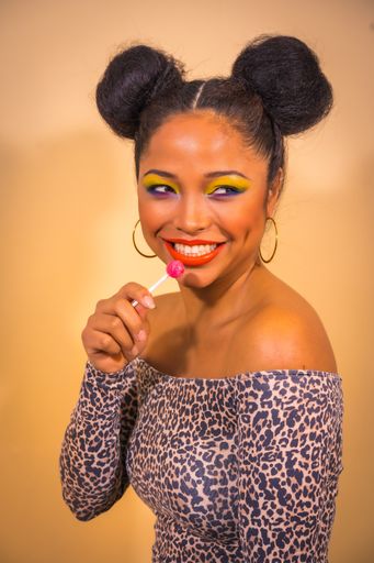 A closeup portrait of a sexy sensual woman with bright makeup and two side bun hairstyle holding a lollipop