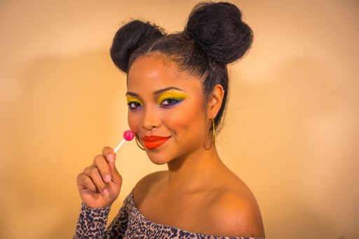 A closeup portrait of a sexy sensual woman with bright makeup and two side bun hairstyle holding a lollipop