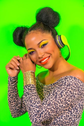 A closeup portrait of a pretty Hispanic woman with bright makeup and two side bun hairstyle listening to music with headphones