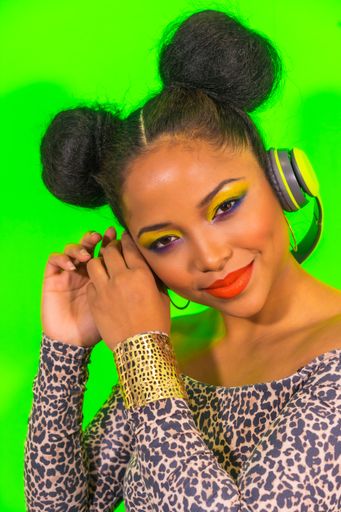 A lovely smiling hipster girl with bright makeup and two tails hairstyle enjoying music with headphones
