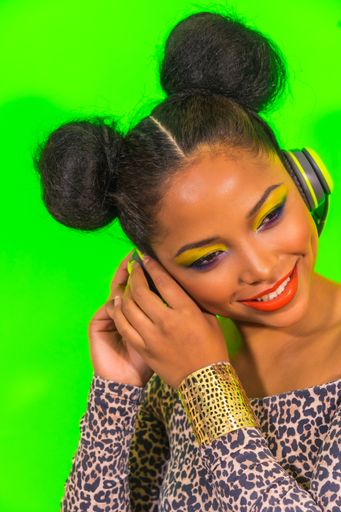 A closeup portrait of a pretty Hispanic woman with bright makeup and two side bun hairstyle listening to music with headphones