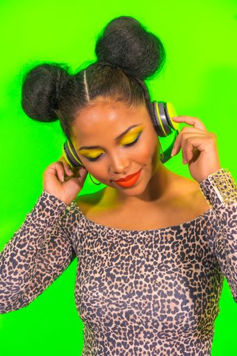 A closeup portrait of a pretty Hispanic woman with bright makeup and two side bun hairstyle listening to music with headphones