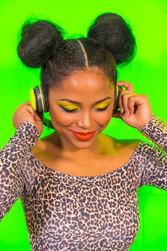 A closeup portrait of a pretty Hispanic woman with bright makeup and two side bun hairstyle listening to music with headphones