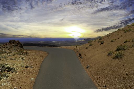 A road surrounded by hills covered in greenery and sand under a cloudy sky during the sunset in Spain