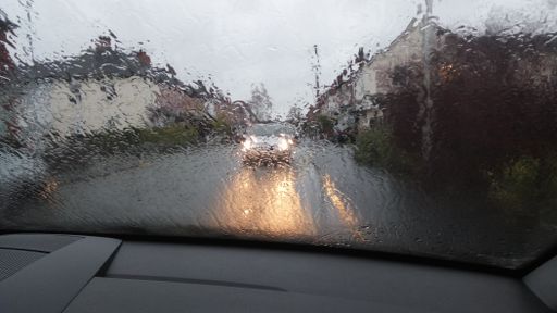 A window covered in raindrops with the road and buildings on the blurry background
