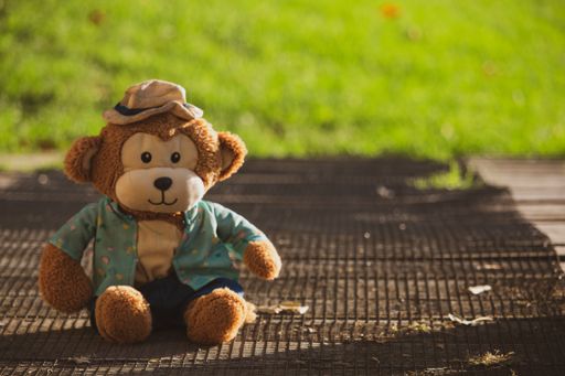 A closeup shot of a soft toy monkey sitting on the ground in the daytimen on the blurred background