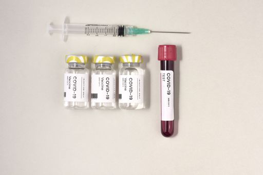 A top view of a syringe needle with the COVID-19 test and vaccine ampoules on the table