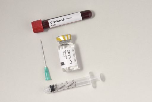 A top view of a syringe needle with the COVID-19 test and a vaccine ampoule on the table