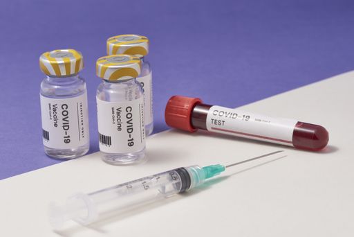 A closeup of a syringe needle with the COVID-19 test and vaccine ampoules on the table