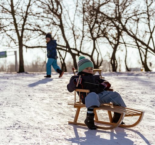 Young three years old Polish Caucasian boy riding a wooden slide on snow at a park on a cold winter day.