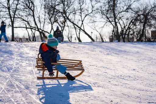 Young three years old Polish Caucasian boy riding a wooden slide on snow at a park on a cold winter day.