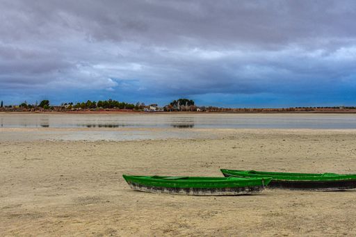 A closeup of two old green fishing boats on a sandy shore of a lake under the clo